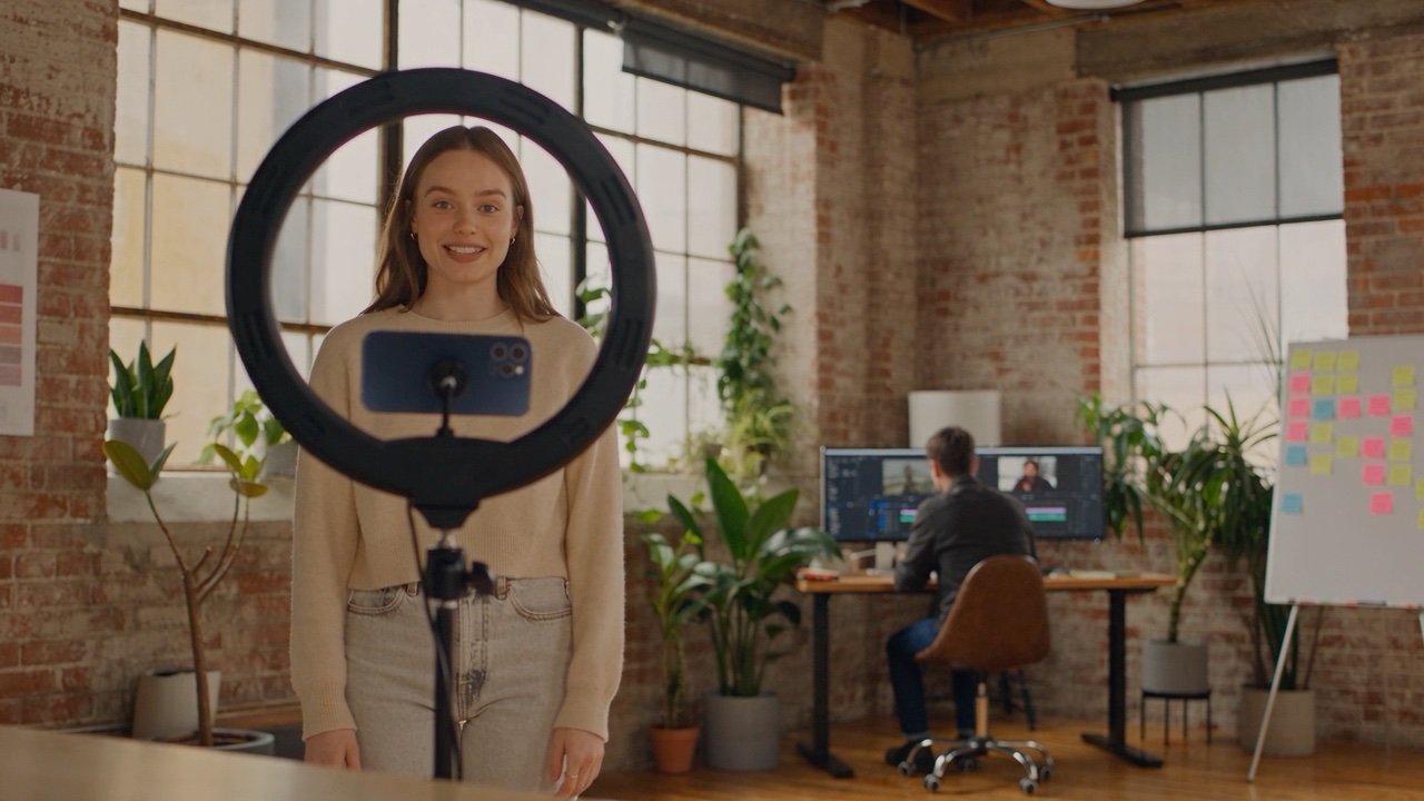 A creator talking to a phone on a tripod inside a ring light; an editor cutting at a desk behind her